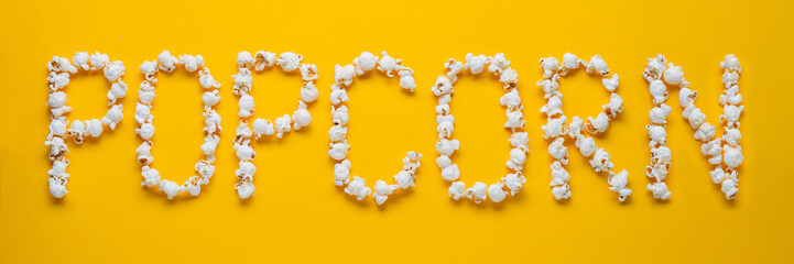 The word POPKORN is laid out from pieces of salt popcorn on a yellow background. Top view. Flat lay - obrazy, fototapety, plakaty