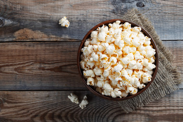 A wooden bowl of salted popcorn at the old wooden table. Top view with copy space. Flat lay. Dark background