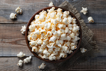 A wooden bowl of salted popcorn at the old wooden table. Top view. Flat lay. Dark background - obrazy, fototapety, plakaty