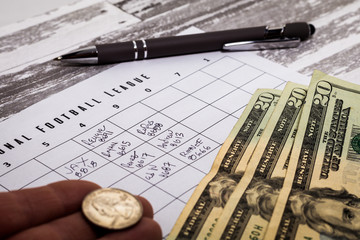 Football office pool grid for sports betting concept with money and a pen, partially completed boxes