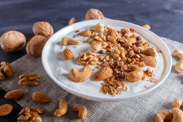 White plate with greek yogurt, granola, almond, cashew, walnuts  on black wooden background.
