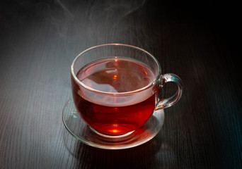 hot black tea in a Cup with steam over it on a dark wooden table