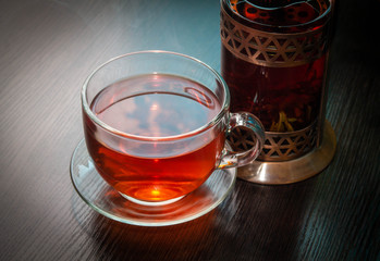 black tea in a Cup close and a glass copper teapot behind it on a wooden table