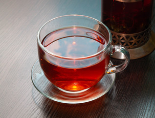 black tea in a Cup close and a glass copper teapot behind it on a wooden table