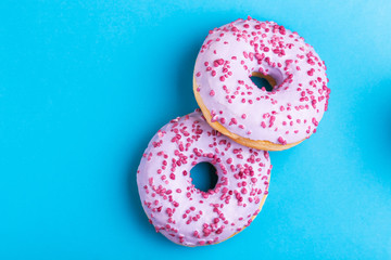Two delicious lilac donuts with sprinkle on bright blue background