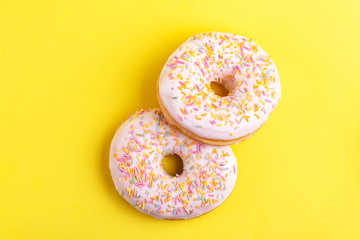 Two delicious vanilla donuts with sprinkle on bright yellow background