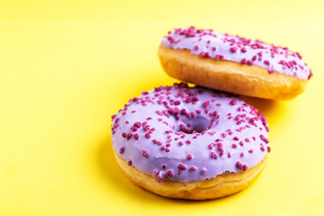 Two delicious lilac donuts with sprinkle on bright yellow background