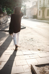 Happy hipster carefree girl in boho outfit with flowers relaxing in evening light in summer city. Stylish bohemian girl walking in sunny street. Back view. Space for text. Summer vacation