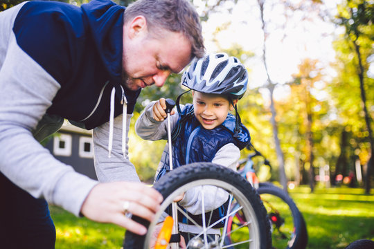 Father's day Caucasian dad and 5 year old son in the backyard near the house on the green grass on the lawn repairing a bicycle, pumping a bicycle wheel. Dad teaches how to repair a child's bike - Powered by Adobe