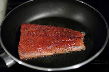 Wild caught Coho salmon frying in a pan with the skin side down.