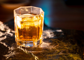 One glass of the whisky on the natural stone plate with shadows