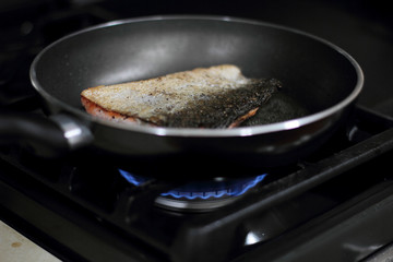 Wild caught Coho salmon frying in a pan with the skin side up.
