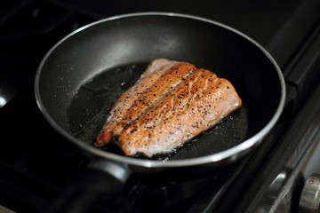 Wild caught Coho salmon frying in a pan on a gas stove.