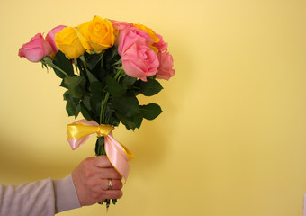 A man holding a bouquet of yellow and pink roses on a light-yellow background. Copy space for text.