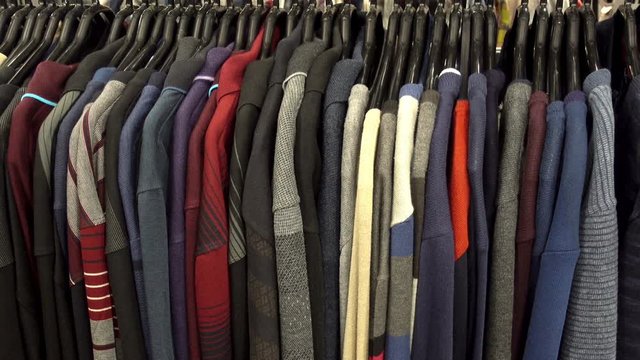 Fashionable collection of warm clothes. Various sweaters hang on hangers on the rack. HD video
