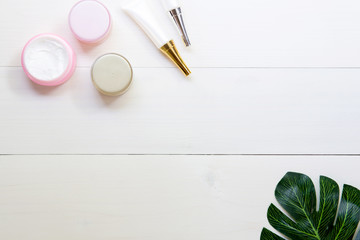 cosmetic and skin care product and green leaves on white wood table, beauty with treatment cream and moisturizing on wooden desk, health and wellness concept, top view.