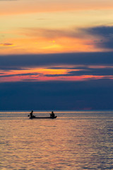 Two men fishing on the sea under sunset.