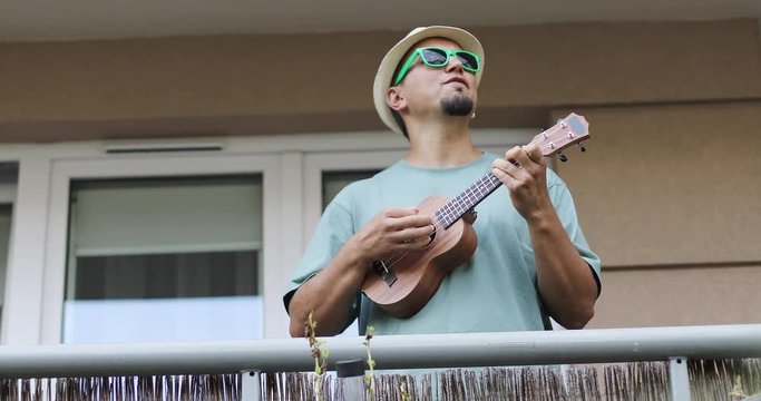Funny man in a hat and sunglasses plays the ukulele.