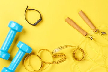 dumbbells, fitness tracker, jump rope and measuring tape on a yellow background, fitness concept
