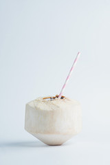 Freshly cut juicy coconut with a straw inside on white background.