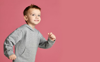 Young baby boy kid in grey hoodie with free text copy space running happy smiling on pink