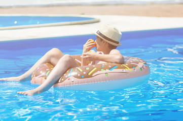 Cute child boy on funny inflatable donut float ring in swimming pool with oranges. Teenager learning to swim, have fun in outdoor pool at resort. Water toys for kids. Healthy sport activity, vacation 