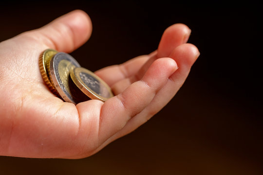 Child holding euro coin in his hand. Pocket money stock image. Poor low income group. Dark background. - Image. Close up.