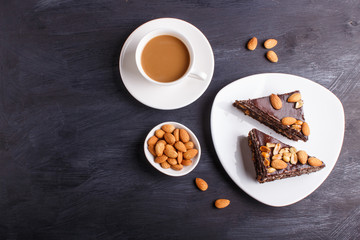 Chocolate cake with caramel, peanuts and almonds on a black wooden background.
