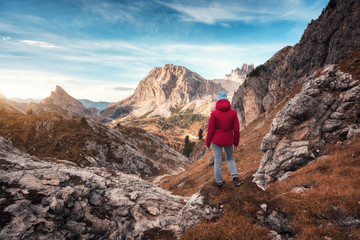 Young woman on the trail looking on high mountain peak at sunset in Dolomites, Italy. Autumn landscape with girl, path, rocks, sky with clouds at colorful sunset. Hiking in alps. Majestic mountains