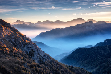 Bergen in mist bij prachtige zonsondergang in de herfst in de Dolomieten, Italië. Landschap met alpine bergdal, lage wolken, bomen op heuvels, dorp in mist, blauwe lucht met wolken. Luchtfoto. Passo Giau