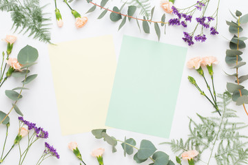 Flowers composition. Paper blank, carnation flowers, eucalyptus branches on pastel  background. Flat lay, top view, copy spaceFlat lay stiil life.