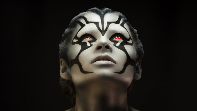 Watchfully looking and intently looking after.Creative appearance of alien creature with red eyes and black and white skin is created through a make-up and body-art