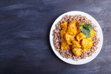 Buckwheat with chicken curry sauce with cashew on black wooden background.