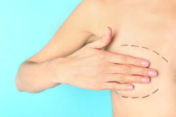 Young woman with marks on breast for cosmetic surgery operation against color background, closeup