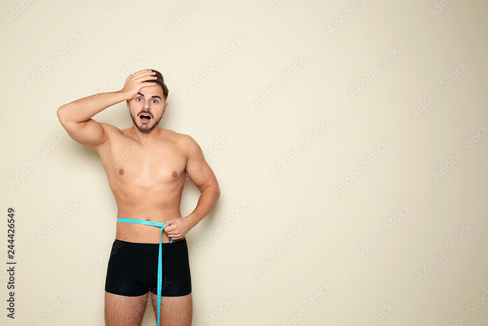 Wall mural fit man measuring his waist on color background, space for text. weight loss