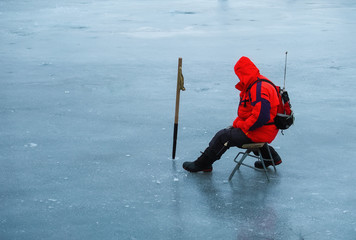 A young man is fishing from a hole on ice. Winter fishing. - Изображение