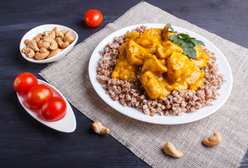 Buckwheat with chicken curry sauce with cashew on black wooden background.