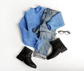 Flat lay composition with jeans, sweater and shoes on white fabric