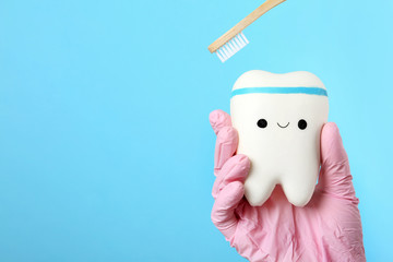 Dentist holding model of tooth with cute face and wooden brush on color background, space for text