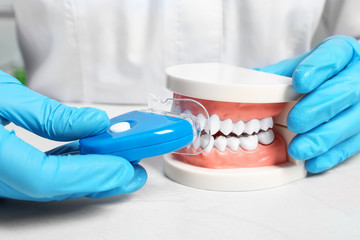 Dentist showing how to use teeth whitening device with educational model of oral cavity at table,...