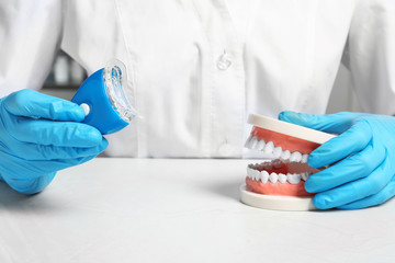 Dentist showing how to use teeth whitening device with educational model of oral cavity at table,...