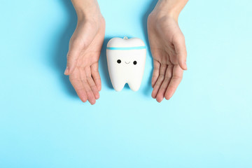 Woman holding hands near model of tooth with cute face on color background, top view. Space for text