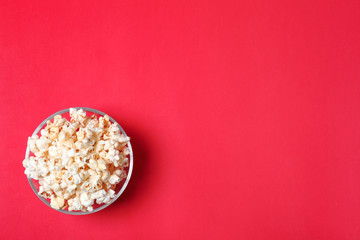 Glass bowl with tasty popcorn on color background, top view. Space for text