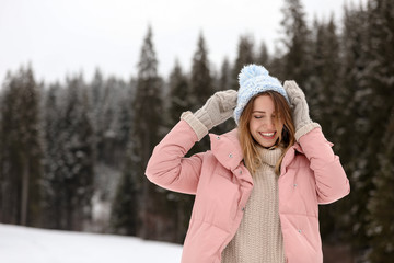 Young woman in warm clothes near forest, space for text. Winter vacation