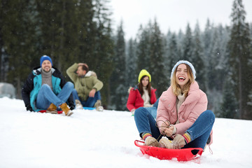 Happy friends sliding on sleds outdoors. Winter vacation - obrazy, fototapety, plakaty