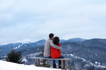 Couple sitting on bench and enjoying mountain landscape. Winter vacation