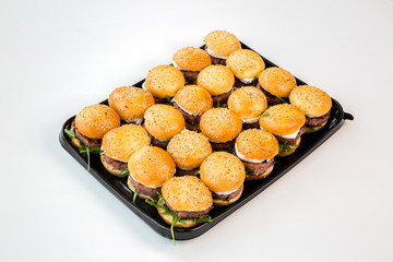 small burgers on a black tray with white background