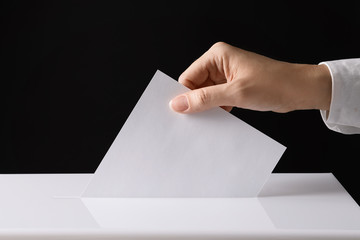 Woman putting her vote into ballot box on black background, closeup