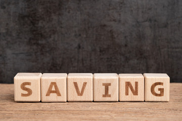 Fototapeta premium Szczęśliwe oszczędności, budżet, inwestycja lub koncepcja celów finansowych, stos kostki drewnianej kostki budującej słowo oszczędzanie na drewnianym stole z ciemnym tłem tablicy z miejscem na kopię