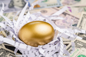Shiny golden egg in paper nest with financial numbers on pile of US dollar banknote money metaphor...